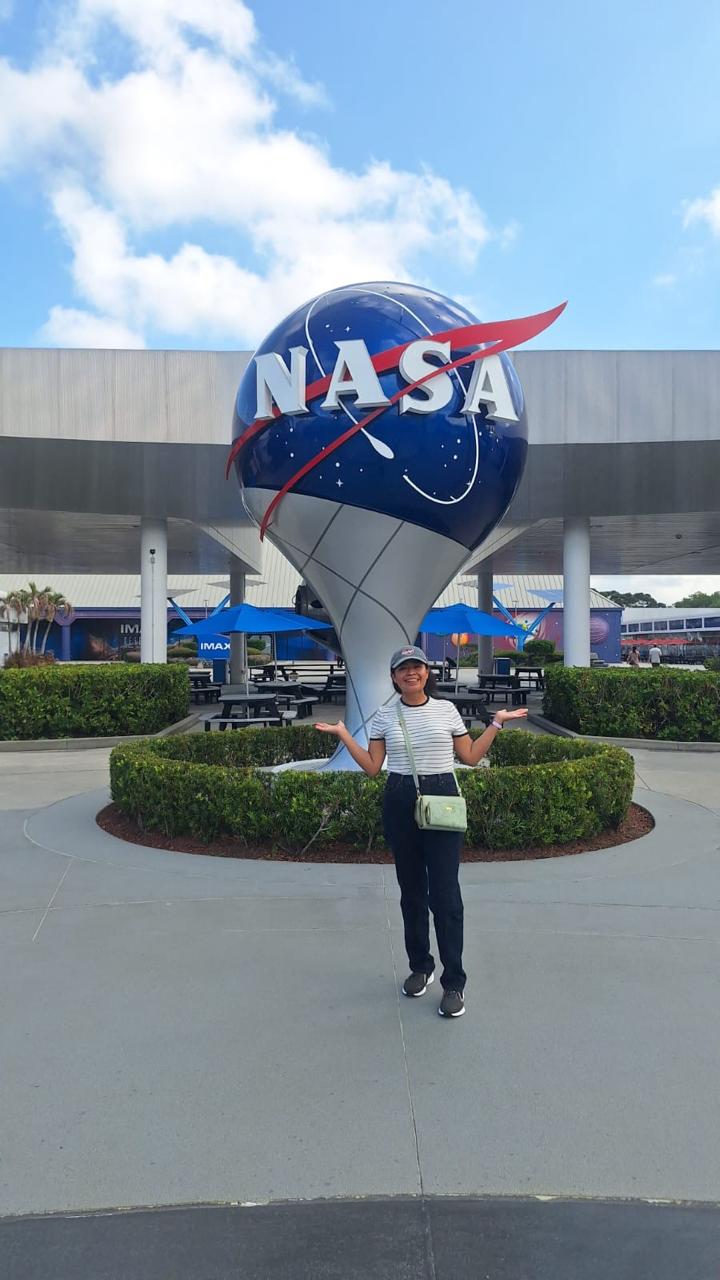 Kelly en el Centro Espacial Kennedy junto al logo de NASA